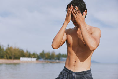 Low angle view of shirtless man with arms raised standing against lake