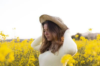 Young woman standing by yellow flowers on field against sky