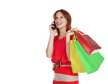 Smiling young woman with shopping bags using phone against white background