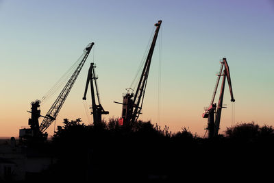 Silhouette cranes at construction site against sky during sunset