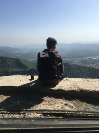 Rear view of man sitting on mountain against sky