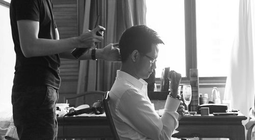 Midsection of male hairdresser spraying on bridegroom hair during wedding