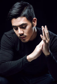 Thoughtful young man looking down against black background