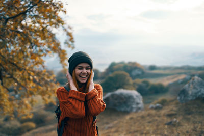 Smiling young woman standing outdoors during autumn against sky