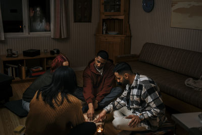 Multiracial friends touching ouija board while ghost seen through window in log cabin