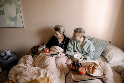 Woman feeding juice to cat while having breakfast on bed with girlfriend at home