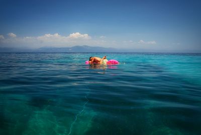 Couple relaxing on inflatable raft in sea against sky