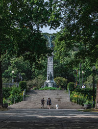 Statue of people walking on road amidst trees in city