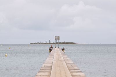 Pier amidst sea against cloudy sky during sunny day