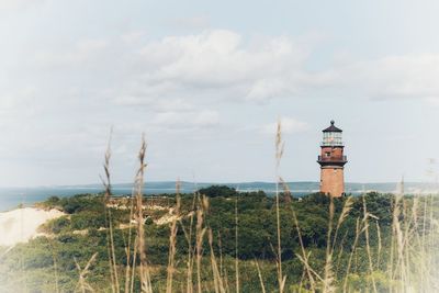 Lighthouse amidst trees and buildings against sky