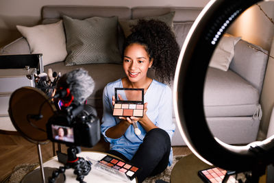 Smiling young woman holding face powder by camera at home