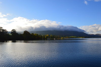 Scenic view of lake with clouds over mountains against sky