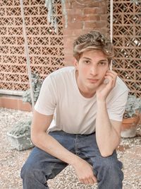Portrait of young man sitting against wall