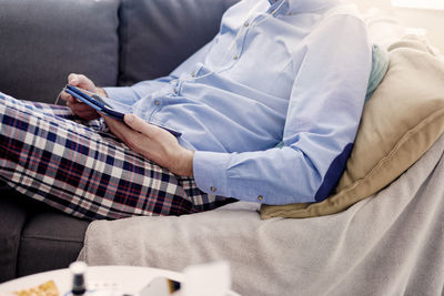 Midsection of man using mobile phone while sitting on sofa