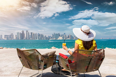 Woman having drink while sitting at beach in city