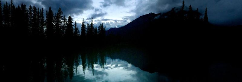Scenic view of lake by silhouette trees against sky at dusk