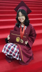 Young woman wearing graduation gown standing against yellow wall