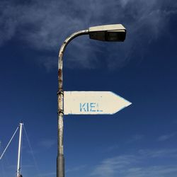 Low angle view of arrow symbol with text on street light against blue sky