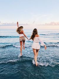 Rear view of women standing at beach against sky