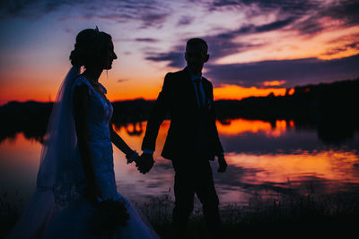 Silhouette people standing by lake against sky during sunset