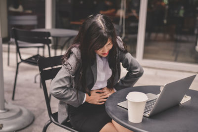 Businesswoman with stomachache using laptop at outdoor cafe