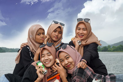 Portrait of smiling friends standing against sky