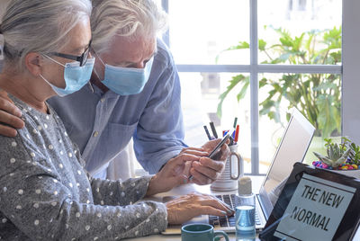 Senior couple wearing mask using laptop at home