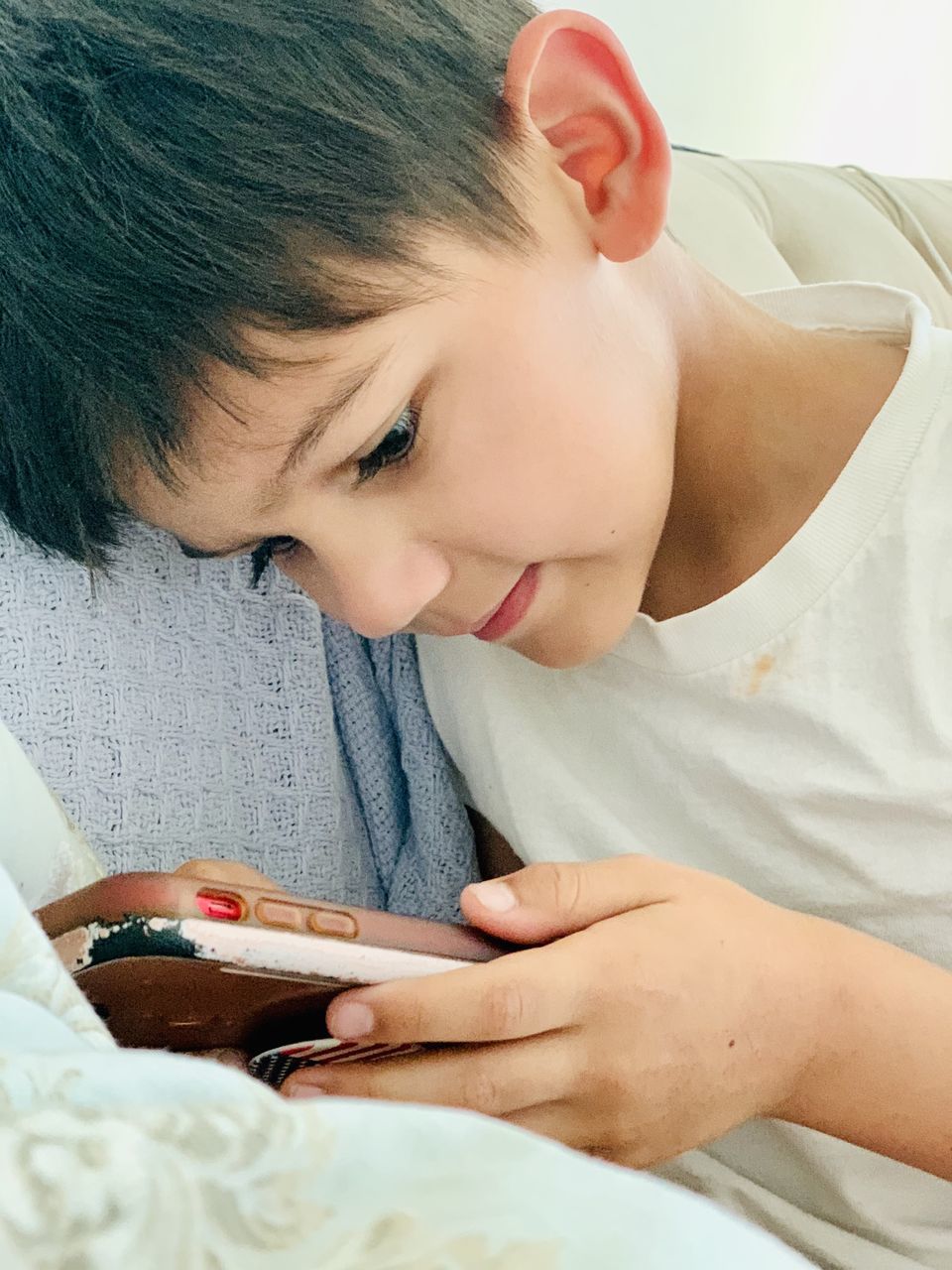 CLOSE-UP PORTRAIT OF BOY HOLDING CAMERA ON BED IN BEDROOM