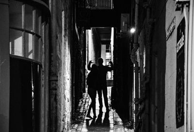 Rear view of woman and man standing in small alleyway at night time