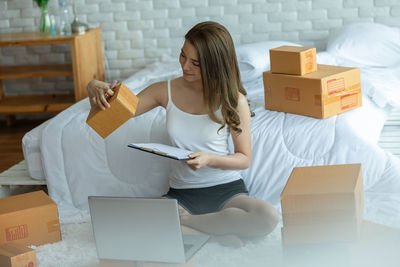 Full length of young woman using laptop while sitting by bed at home