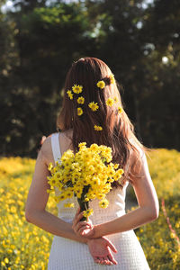 Rear view of woman holding flowers standing at field