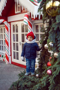 Child boy in a jacket stands next to the house of sweets at a fair in moscow for the new year 2020