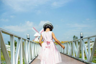 Woman standing on railing against sky