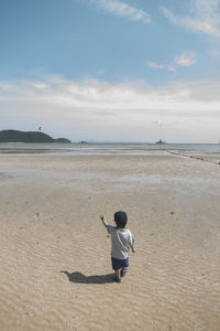 Rear view of boy standing on beach against sky