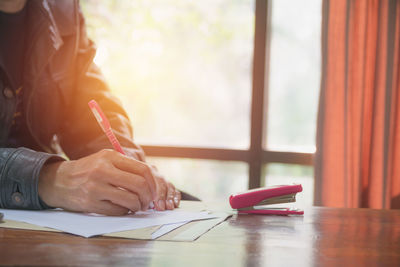 Midsection of person writing while holding led bulb on table