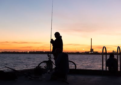 Silhouette of people fly-fishing on jetty in river during sunset