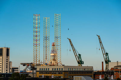 Low angle view of cranes against clear blue sky