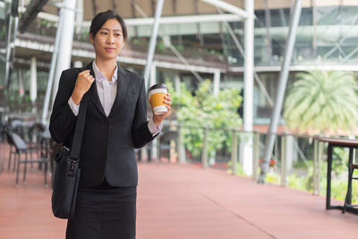 Businesswoman holding disposable cup while standing against building in city