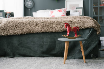 Vintage wooden toy horse stands on a stool in the bedroom near the bed in dark colors