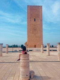 Rear view of woman sitting outside building against sky