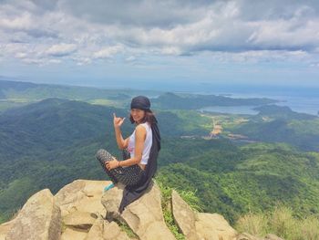 Young woman sitting on rock against sky