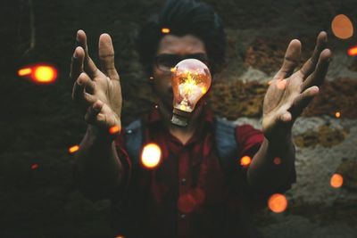 Digital composite image of man with levitating light bulb against brick wall