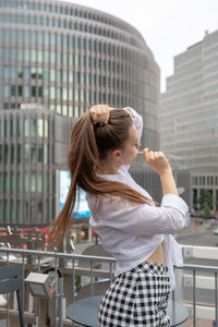 Young woman eating lollipop while standing by buildings in city
