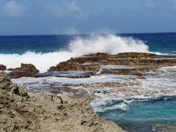 Waves splashing on rocks at shore against sky