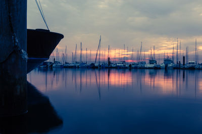 Sailboats moored at harbor against sky during sunset