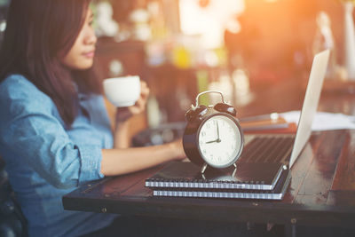 Alarm clock on notepads with female blogger working in background at cafe table