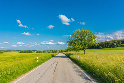 Empty road amidst field against sky