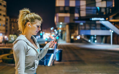 Side view of young woman using mobile phone in city