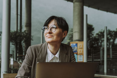 Smiling businesswoman with laptop sitting at sidewalk cafe