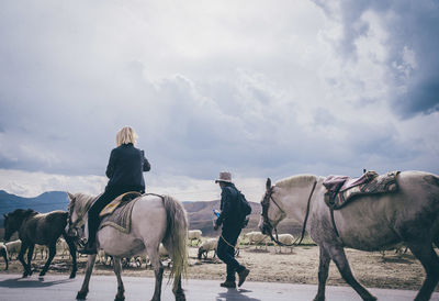 People riding horses on shore against sky